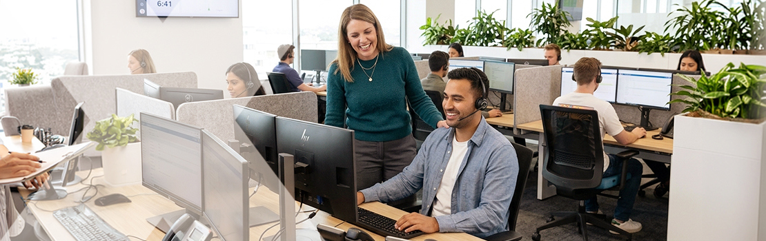 A manager showing how specific praise is a good staff recognition idea, smiling with their hand on a customer service agent's shoulder in a modern call centre