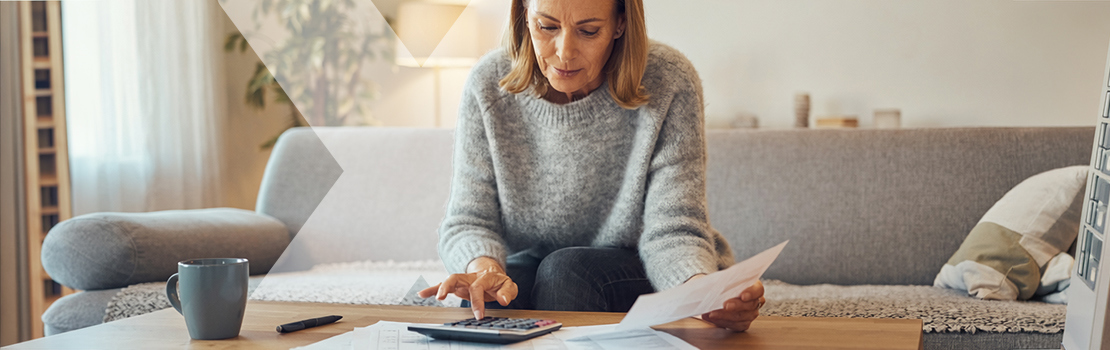 A person sitting on a sofa at home, using a calculator to calculate their usual cost of commuting to work