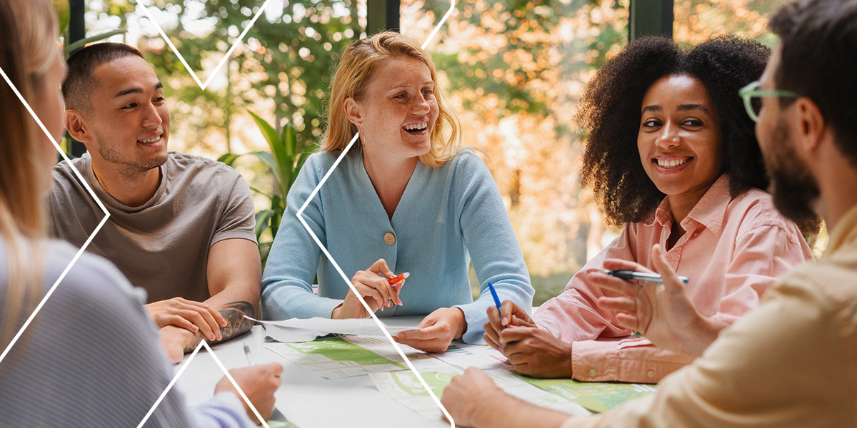 Employees sitting around a communal office table and laughing, showing the impact of a positive employee lifecycle on employee engagemen